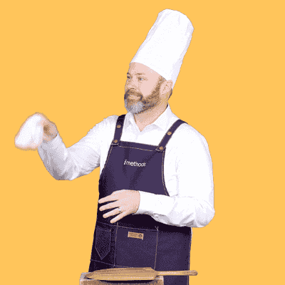 Pat in a chef's hat and apron tossing pizza dough into the air in front of a yellow background